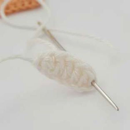 White crochet knot strip with a needle threading its tail through the opposite end