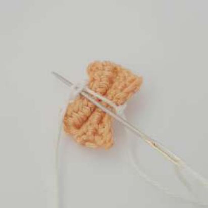 Needle threading the yarn ends through the middle loops at the back of a crochet bow tie