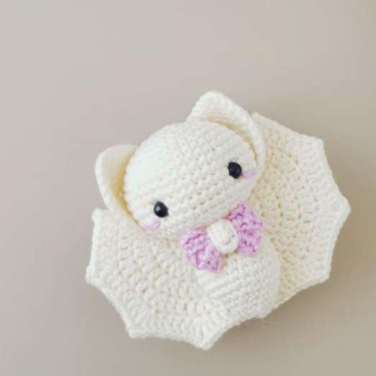 Cream crochet baby bat with an orchid bow tie and pink blush, wings spread open