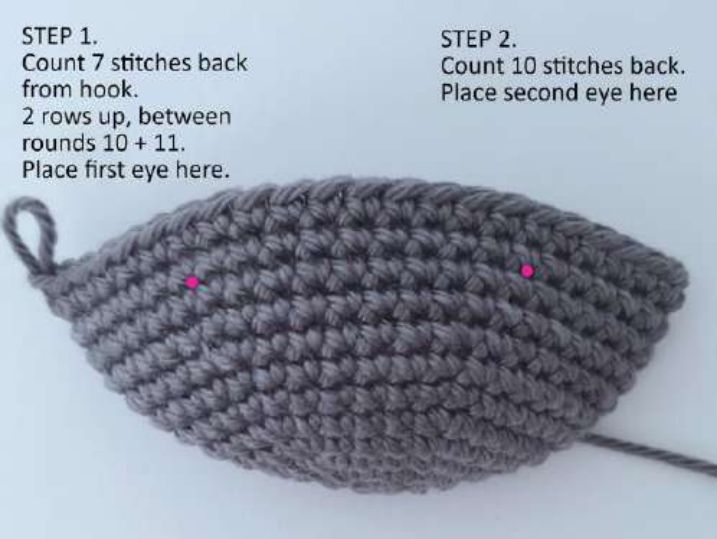 Crochet bat head after round 12 with two pink markers where the safety eyes go, between rounds 10 and 11