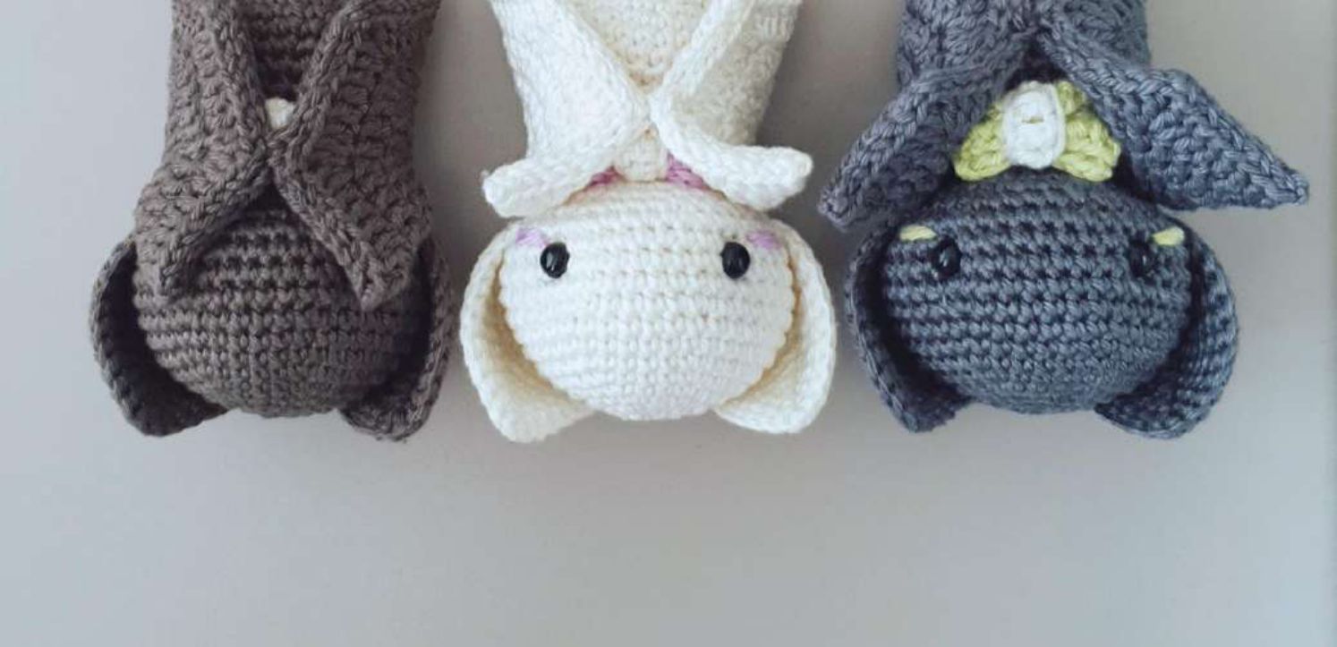 Three crochet baby bats hanging upside down with folded wings, in brown, cream and charcoal