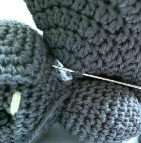 Needle attaching a crochet wing to the side of the body near the ear