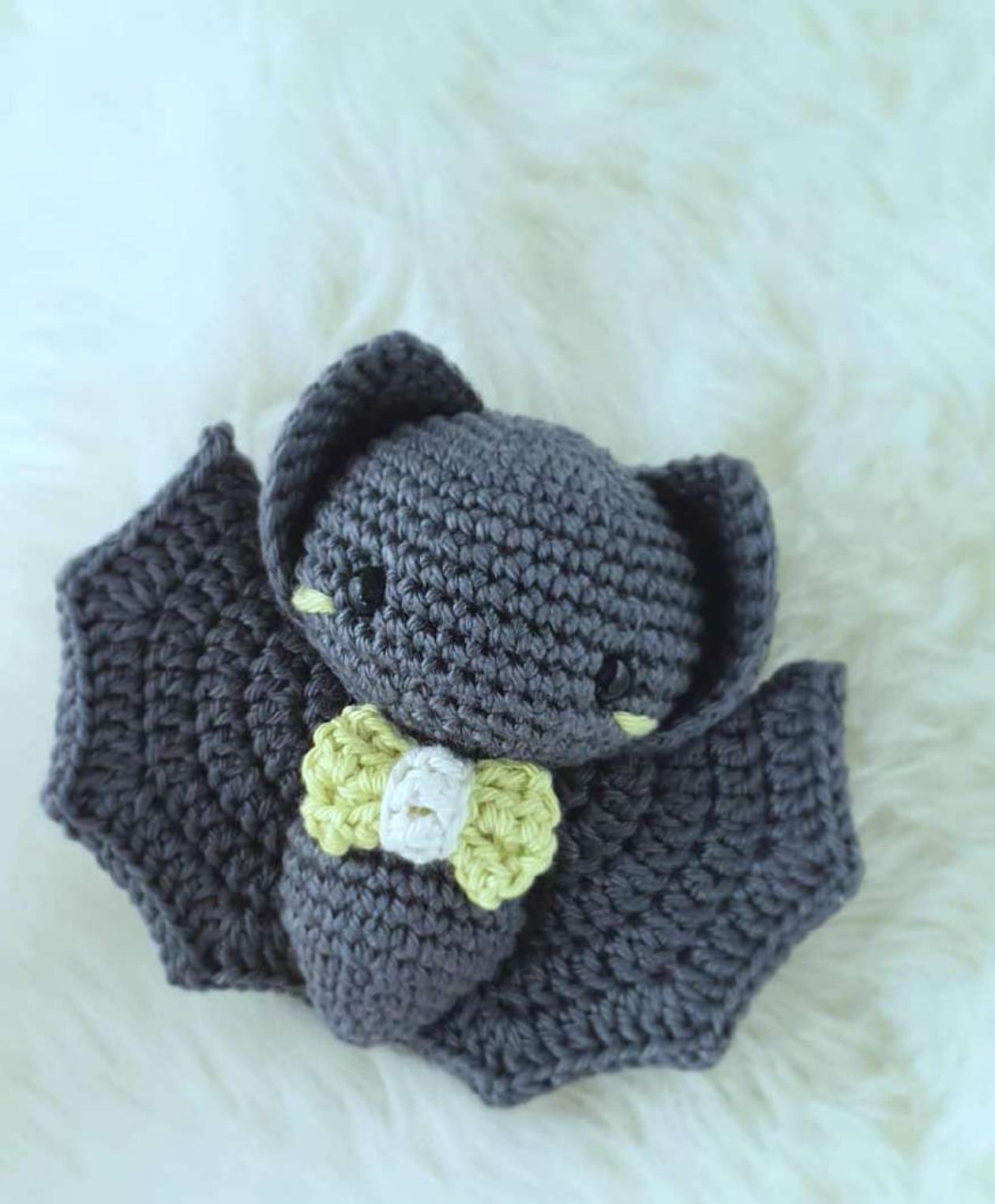 Charcoal crochet bat with scalloped wings, triangular ears and a lime bow with a white center.