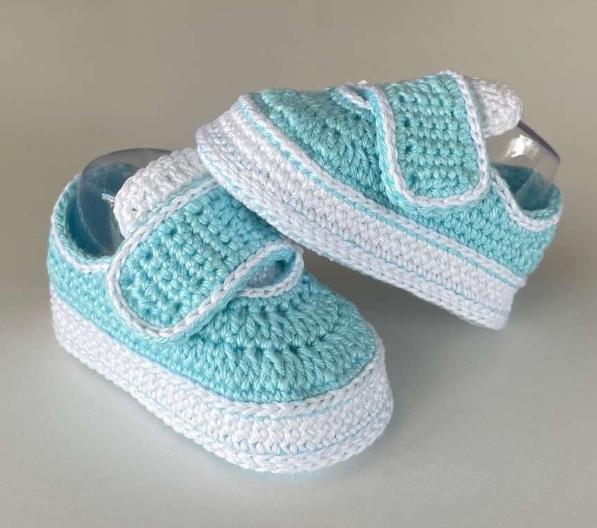 A pair of aqua crochet baby sneakers with white reinforced soles and fastening straps.