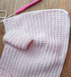 Crochet hook at the top corner of the pink cardigan front, working the band