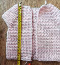 Measuring tape laid down the front of the pink crochet cardigan from the shoulder