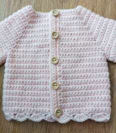 Pink crochet baby cardigan with wooden buttons and a shell edging at the hem