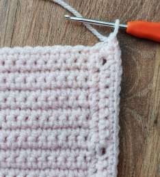 Crochet hook joining yarn at the bottom corner of the pink cardigan band