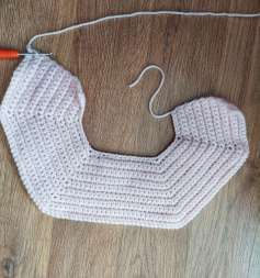 Flat pink crochet yoke in single crochet, shaped like a wide U, hanging from a hanger