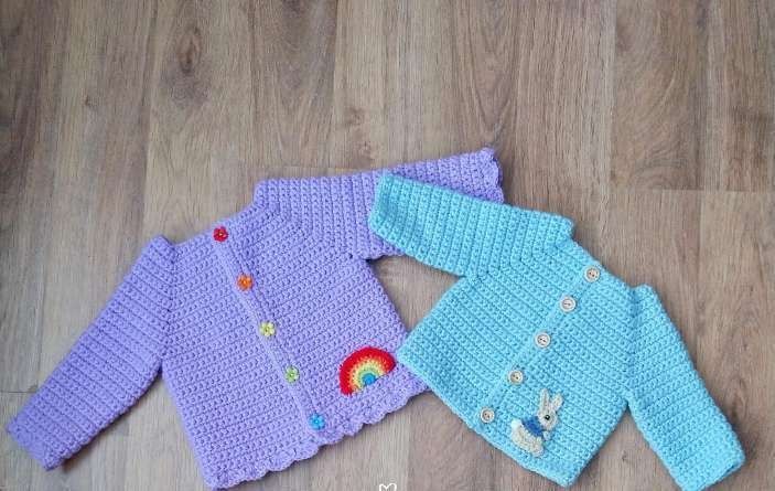 Lavender crochet baby cardigan with a rainbow applique next to a blue one with a bunny applique