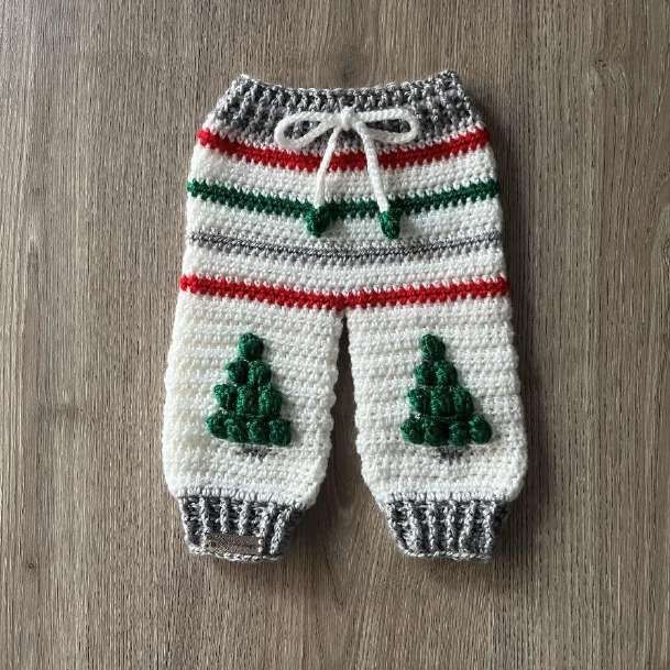 White crochet baby pants with red, green and gray stripes, gray ribbing and a green bobble tree on each leg.