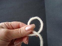 Hand holding a loop of cream yarn to start a magic circle