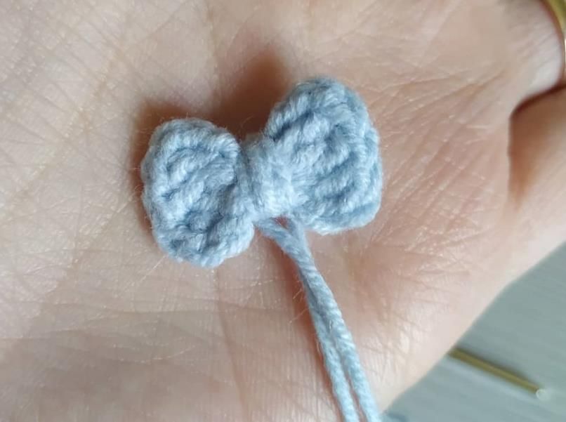 Small light blue crochet bow wrapped in the middle, with a yarn tail