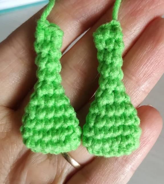 Two long green crochet frog legs with flattened tops, held in a hand
