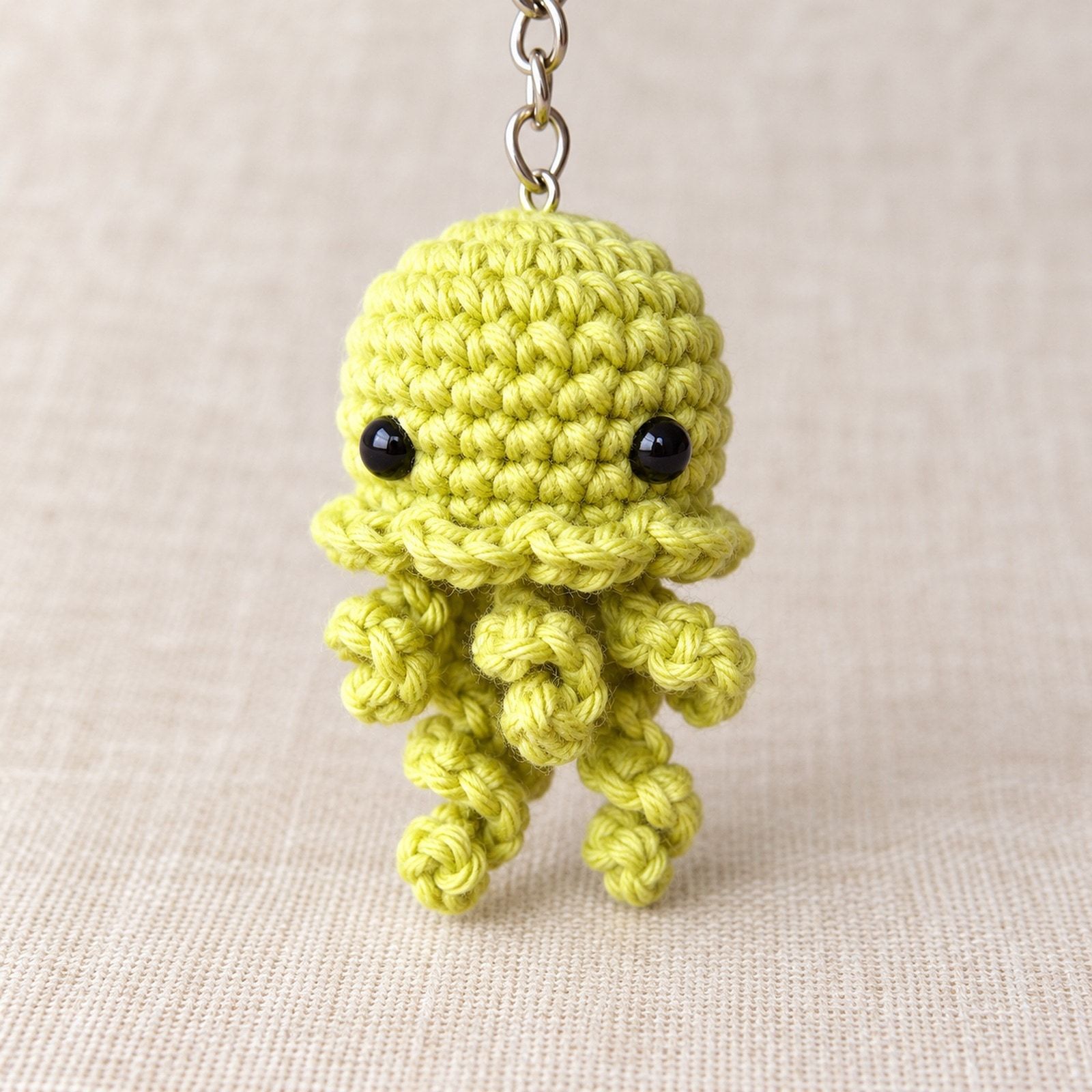 Yellow-green crochet jellyfish with two black eyes, a ruffled edge and five curled tentacles.