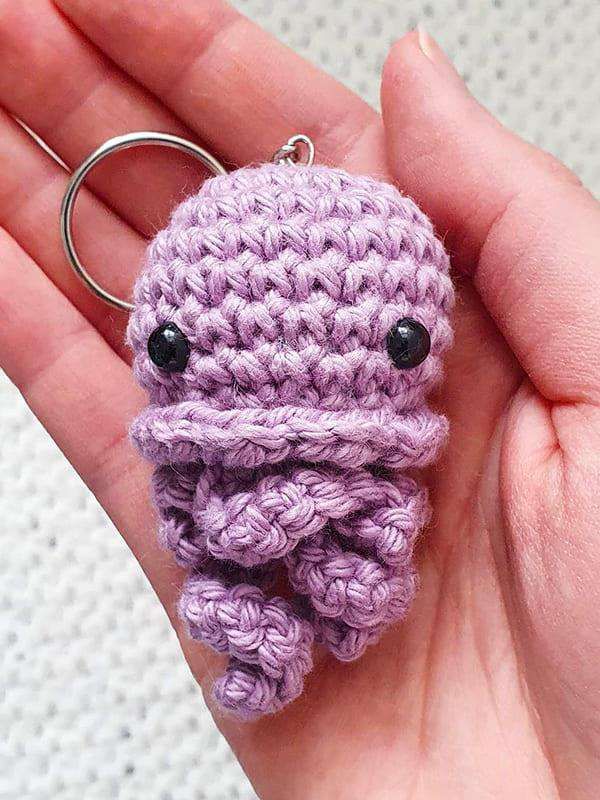 Lilac crochet jellyfish keychain with a ruffled skirt and curly tentacles, held in a hand