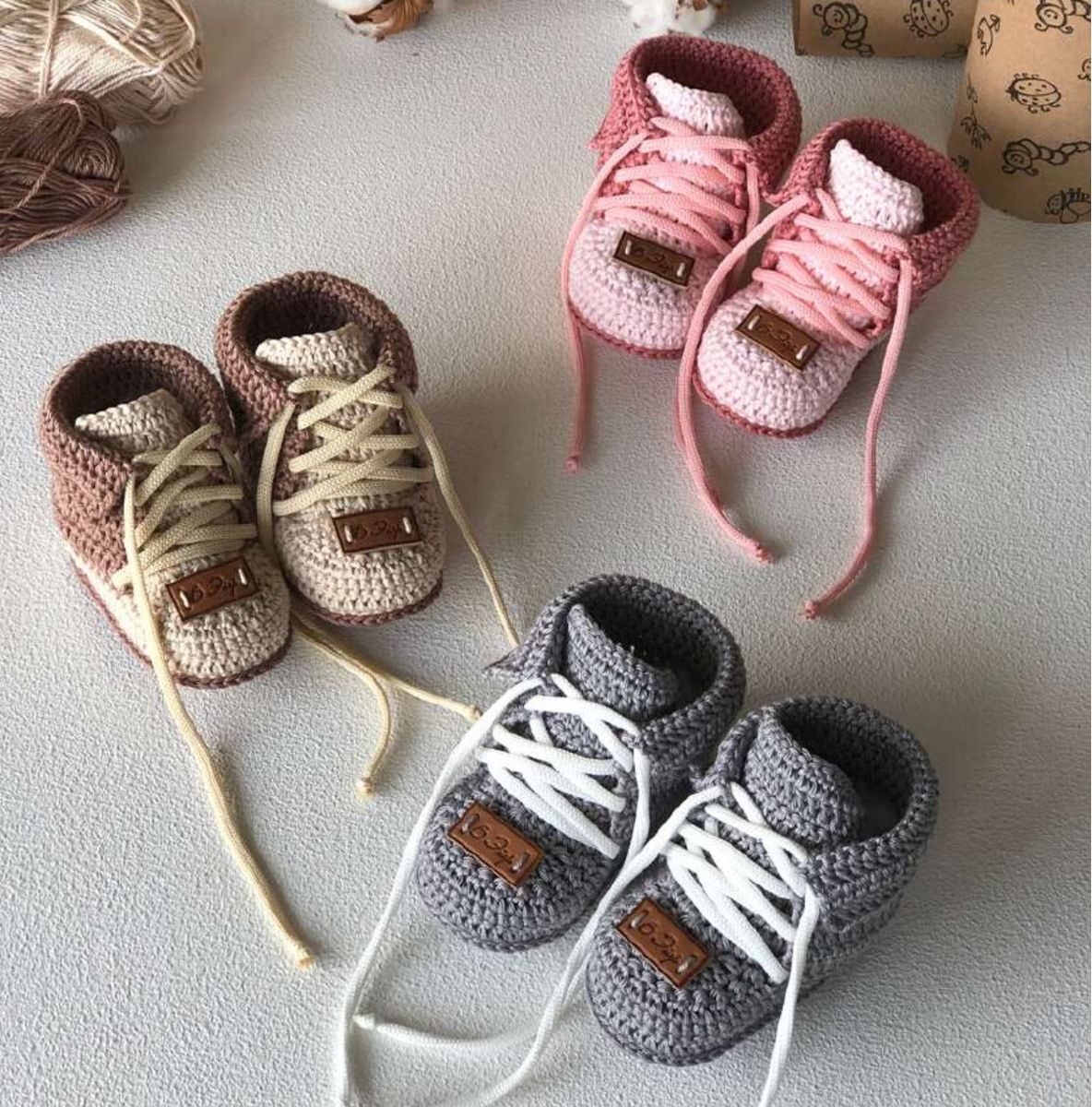 Three pairs of crochet baby shoes in pink, brown and gray, with folded cuffs and threaded laces.
