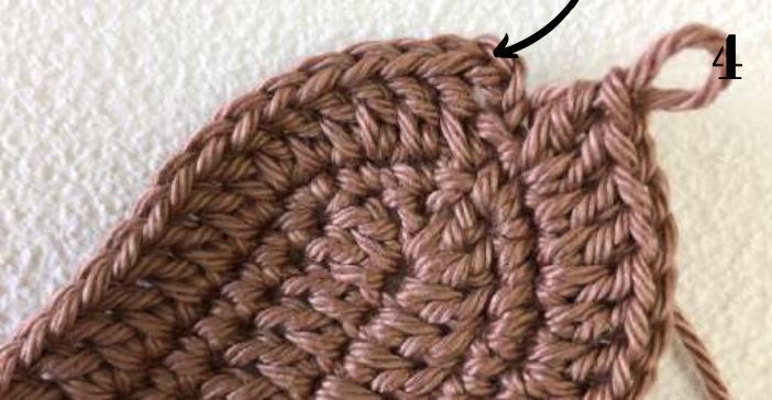 Rounded end of the brown crochet sole with an arrow at the join of round 3