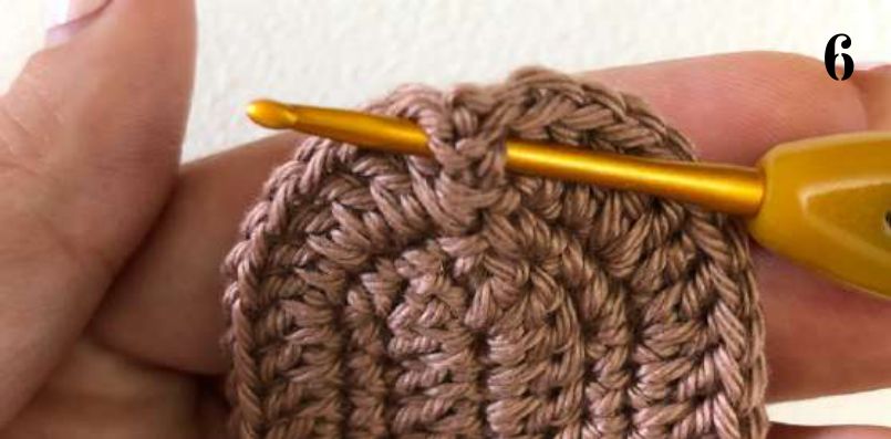 Crochet hook working beige yarn around the post of a stitch at the edge of the brown sole