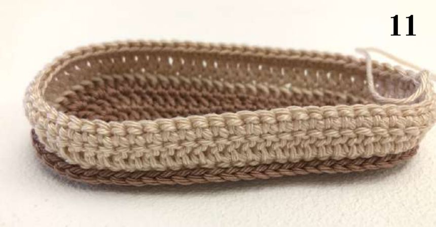 Crochet shoe base with beige sides on a brown sole and a yarn tail, ready for the toe