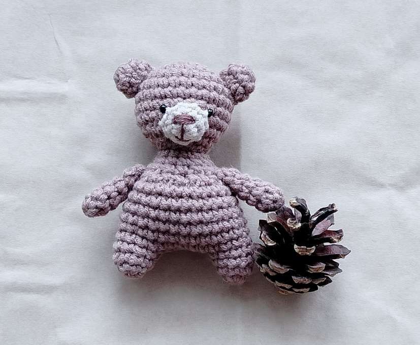 Taupe crochet teddy bear holding a pine cone