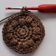 Brown crochet circle with a red hook starting a bobble stitch