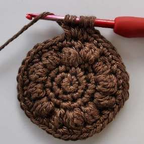 Several loops of brown yarn on a red crochet hook while making a bobble stitch