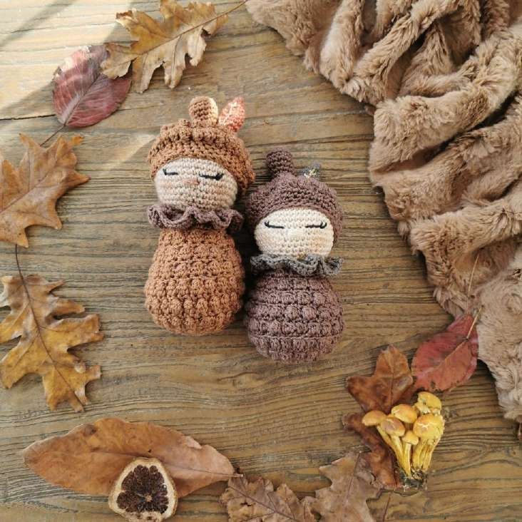 Two crochet pine cone baby dolls with sleepy faces, bobble stitch bodies and caps, on autumn leaves